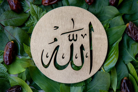 Name of Allah in arabic on gold wood, green leaves and dates fruit background. Calligraphy means the God Al Mighty of Islam Religion.の写真素材