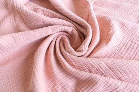 Soft muslin baby blanket background. Cotton clothing and textiles. Natural organic fabrics texture. Light pink rose color. Close up.の写真素材