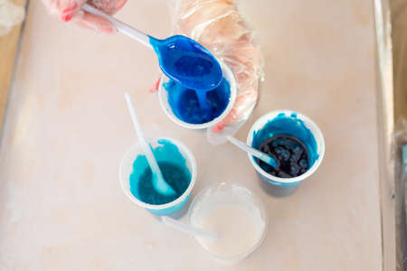 Epoxy resin different blue color in cup for casting stabilizing wood, abstract art. Process of making accessory from resin.Mixing colorful of resin chemical in plastic cupの写真素材