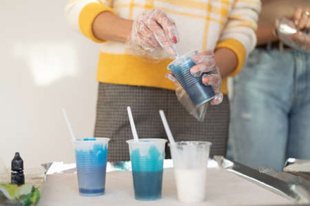 Epoxy resin different blue color in cup for casting stabilizing wood, abstract art. Process of making accessory from resin.Mixing colorful of resin chemical in plastic cupの写真素材