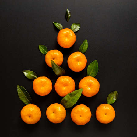 Christmas tree made of orange mandarins and green leaves, on black background. Flat lay, top view, copy space. New Year sale card. Minimal creative conceptの写真素材