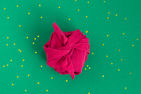 Paper free gift wrapping technique Furoshiki. Viva magenta fabric on green background. Flat lay, present box, top view. Christmas, valentines, new year concept.の写真素材