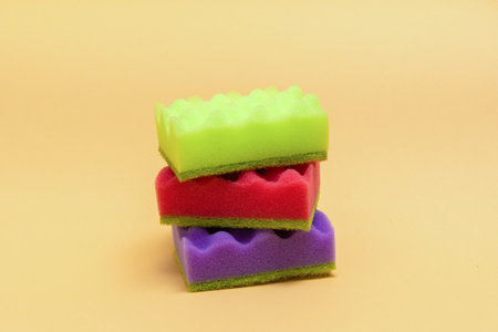 Stack of many multi-colored dish wash sponges pastel orange background. Household cleaning scrub pad. Home cleaning concept. Space for textの写真素材