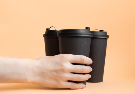 Hands holding paper coffee cups on orange background. Take away food conceptの写真素材