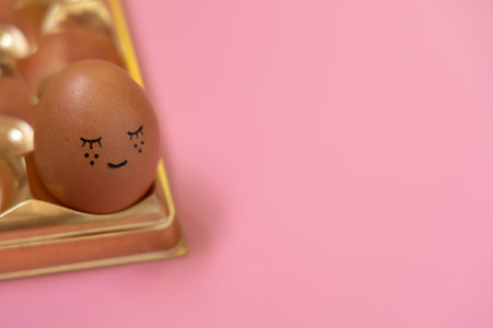 Happy Easter holiday. Cute easter egg in golden box on pastel pink background. Homemade ornament lovely face. Creative arrangement .の写真素材