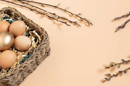 Easter eggs natural and gold in basket with paper filler . Branch of willow catkinsan. Light pastel orange background with copy space.の写真素材
