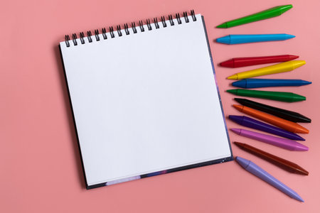 Open sketchbook with white empty blank. Colorful wax crayons on the pastel pink background. Flat lay compositionの写真素材