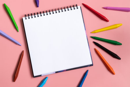 Mock up of empty scketchbook white paper on pastel pink background. Colorful wax crayons. Top view of open notebook with clean sheet. Template art. Copy spaceの写真素材