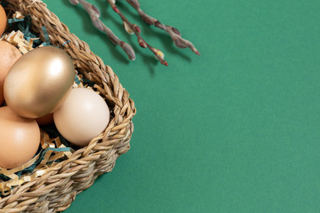 Easter eggs with funny face natural and gold in basket with paper filler . Branch of willow catkins. Light pastel orange background with copy space.の写真素材