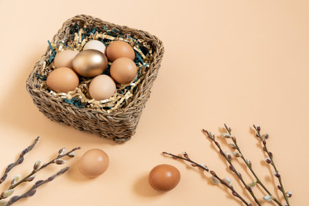 Easter eggs natural and gold in basket with paper filler . Branch of willow catkins. Light pastel orange background with copy space.の写真素材