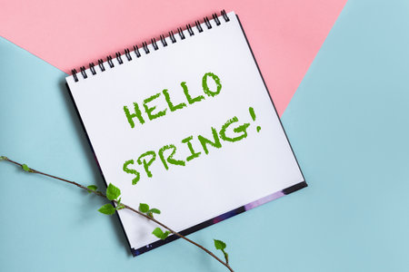 Hello spring message spiral scketchbook white paper on pastel pink and blue background. Twig with fresh leaves. Spring is coming concept.の写真素材