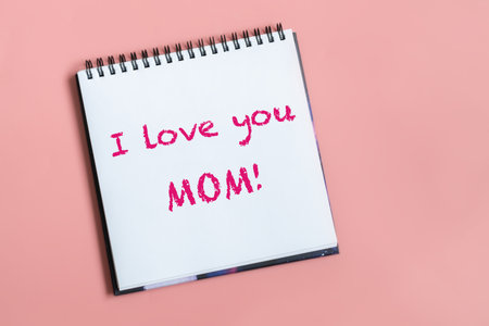 Text words I love you mom on sheet of paper. Happy mothers day concept. Pastel pink background.の写真素材