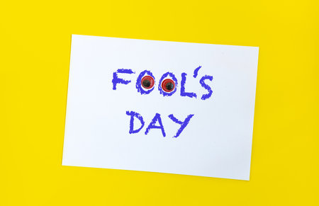 Text word Fool's day on sheet of paper with funny eyes and. 1 april message handwritting on sheet of paper. Bright yellow background. International humor day.の写真素材
