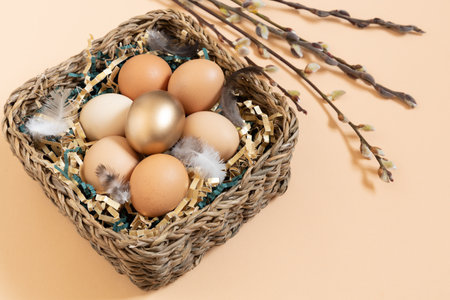 Easter eggs natural and gold in basket with feather. Branch of willow catkins. Light pastel orange background with copy space.の写真素材