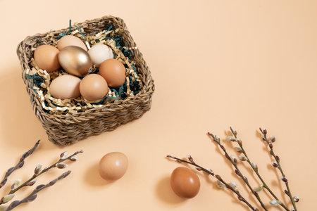 Easter eggs natural and gold in basket with paper filler . Branch of willow catkins. Light pastel orange background with copy space.の写真素材