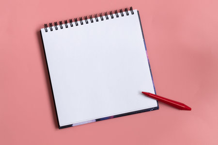 Mock up of empty scketchbook white paper on pastel pink background. One red wax crayon. Top view of...