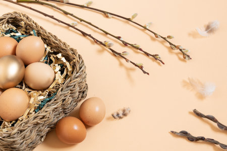 Easter eggs natural and gold in basket with paper filler . Branch of willow catkinsan feather. Light pastel orange background with copy space.の写真素材