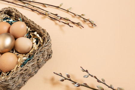 Easter eggs natural and gold in basket with paper filler . Branch of willow catkinsan. Light pastel orange background with copy space.の写真素材