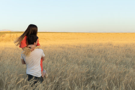 A young man picked up his woman in his arms and carries her on sunset in wheat field.の写真素材