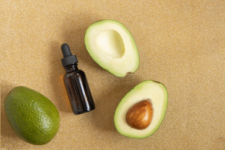 Avocado oil. Essential oil in dark glass bottle on shiny gold background. Avocado for healthy skin and hair. Cosmetics ingredients.の写真素材