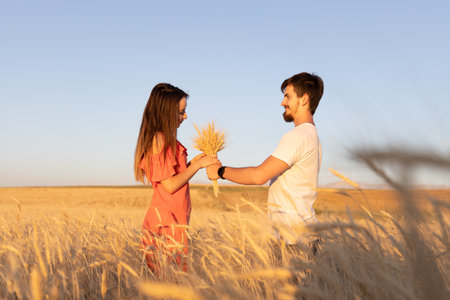 Young couple in the wheat field, The woman is grabbing bouquet of dry wheat, summer time.の写真素材