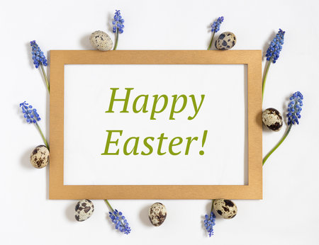 Easter composition with paper blank with text Happy easter, quail eggs, fresh flowers and golden frame.Top view, flat layの写真素材