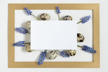 Easter composition with paper blank with text Happy easter, quail eggs, fresh flowers and golden frame.Top view, flat lay.の写真素材