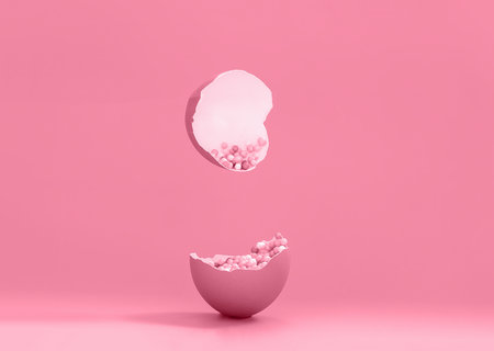 Broken decorative easter egg with colorful confetti. Minimal composition, monochromatic color pastel pink background. Space for textの写真素材