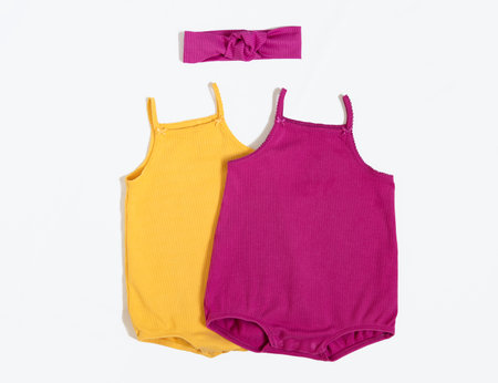 Summer outfit. Baby vest bodysuit yellow and pink color with head accessories. Top view, flat lay on white.の写真素材