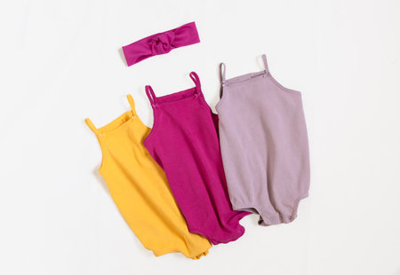 Cute kids summer outfit. Three baby vest bodysuit yellow, pink, lilac color with head accessories. Top view, flat lay on white.の写真素材