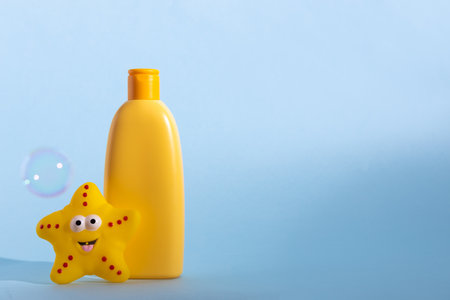 Yellow plastic bottle with baby cosmetic and funny bath toy. Soap bubbles on a background. The concept of childrens bath time.の写真素材