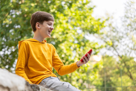 Happy smiling teen boy talking on video call using phone outside.の写真素材