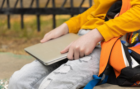 Teenager boy resting in a park after school. Holding a laptop on a sunny day, outdoors.の写真素材