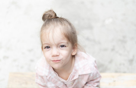 Close-up portrait of a young girl on a light background, gazing directly into the camera. Her innocent expression and soft natural light create a gentle and heartfelt moment.の写真素材
