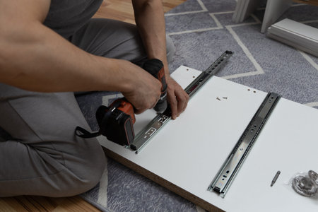 Man using a power screwdriver to assemble a wardrobe at home, close-up of hands and tools. Concept of DIY and home renovationの写真素材