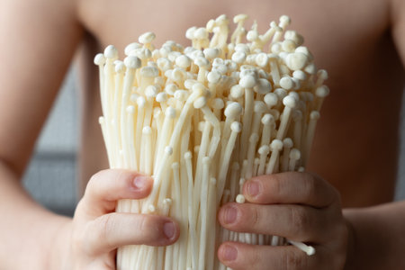 Child gently holding fresh enoki mushrooms. Concept of natural food, curiosity, organic farming, and healthy eating from early childhood.の写真素材