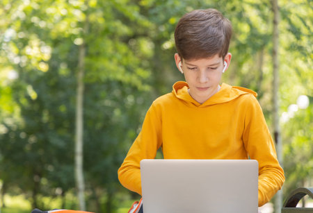 Thoughtful teenager boy working on laptop. Holding and using a laptop for networking on a sunny...