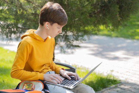 Thoughtful teenager boy working on laptop. Holding and using a laptop for networking on a sunny spring day, outdoors.の写真素材