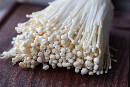 Group of fresh enoki mushrooms lying on a dark textured wooden background. Natural and simple food...