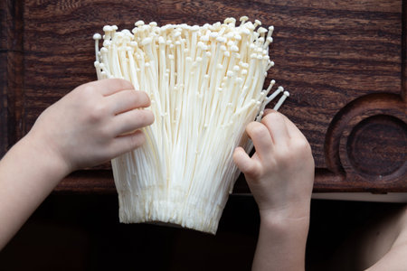 Fresh enoki mushrooms on wooden cutting board, childrens hands touching them, concept of sensory play, food education, and healthy eatingの写真素材