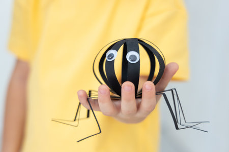 Close up of a paper spider craft made by child and held in hand, diy halloween decoration, handmade art for kids.の写真素材