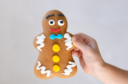 Close up of a gingerbread man cookie held in a child hand on light background with copy space. Sweet holiday concept for Christmas or childhood theme.の写真素材