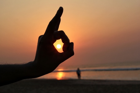 Close up of a hand silhouette capturing the sun set within the fingersの写真素材