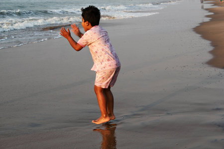 A kid playing in a beach and jumping with joy waiting for the waves to  touch his feetの写真素材