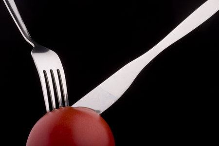 Knife with forks help slices juicy  tomato.