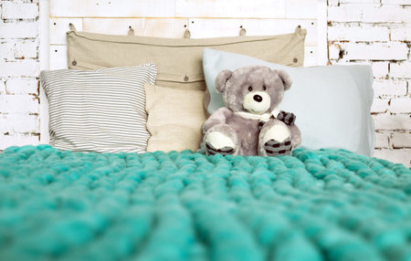 Merino wool blanket on bed with pillows in pastel colors and Teddy bear, loft interiorの写真素材