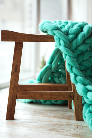 Green knitted merino wool blanket on wooden chairの写真素材