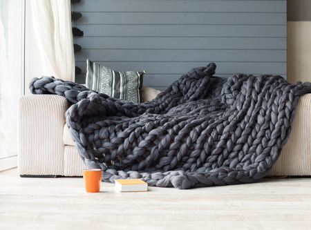 Merino wool grey blanket lying on white sofa with an orange cup and book near itの写真素材