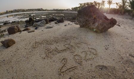 The inscription on the sand of Marsa Alam 2020 at low tide against the backdrop of hotels and reef with sun flareの写真素材