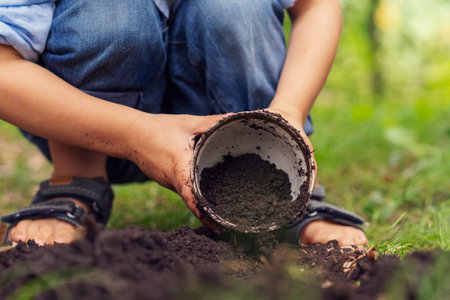 Close-up of a boy digging with a bucket in the garden for planting a plantの写真素材